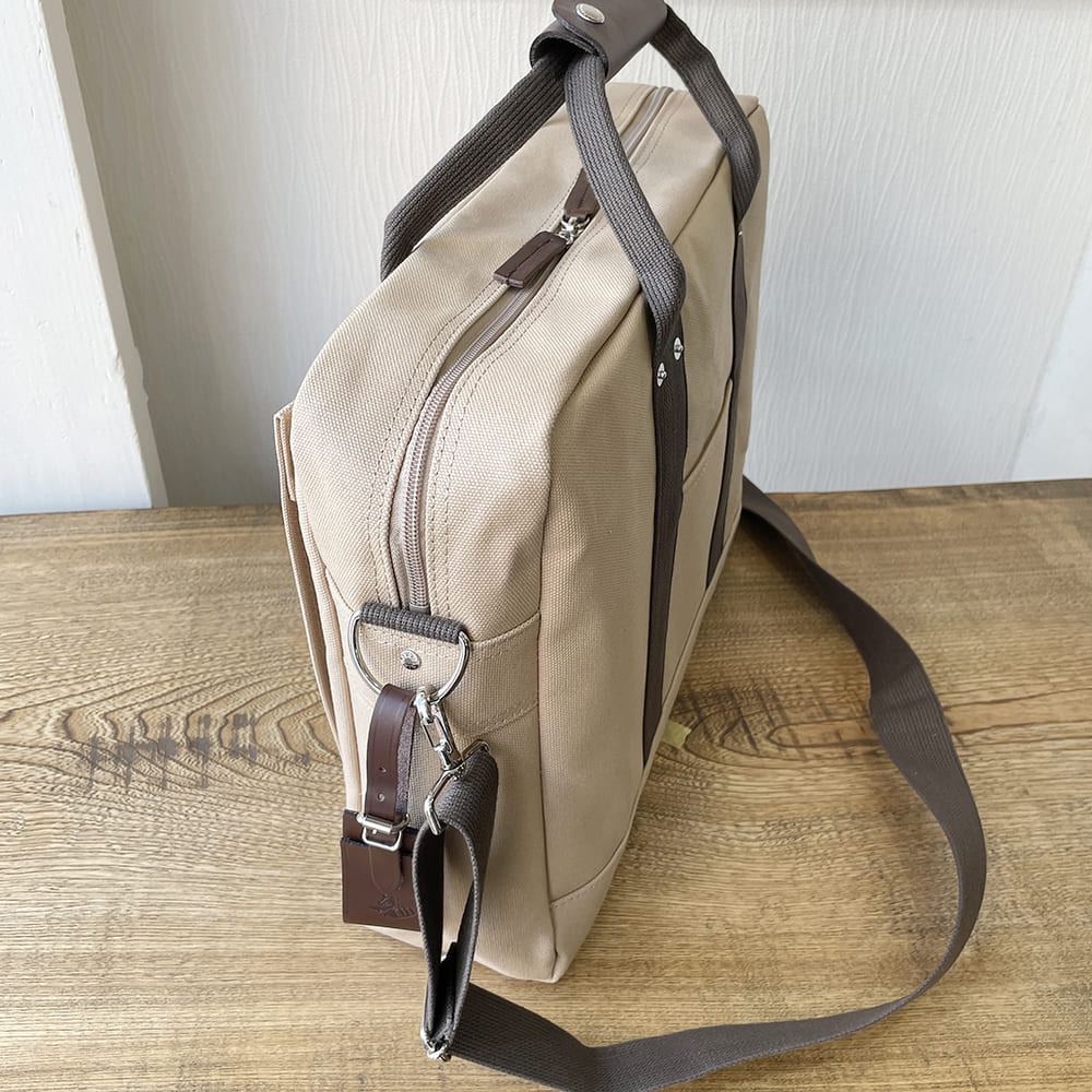 犬印純綿帆布商務公事包，米褐色，配有棕色皮革提把與肩帶，B4尺寸，側邊有拉鍊開口。