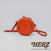 橘色皮革小圓包，圓形包身，正面有半圓形拉鍊開口，兩側有皮革肩帶。