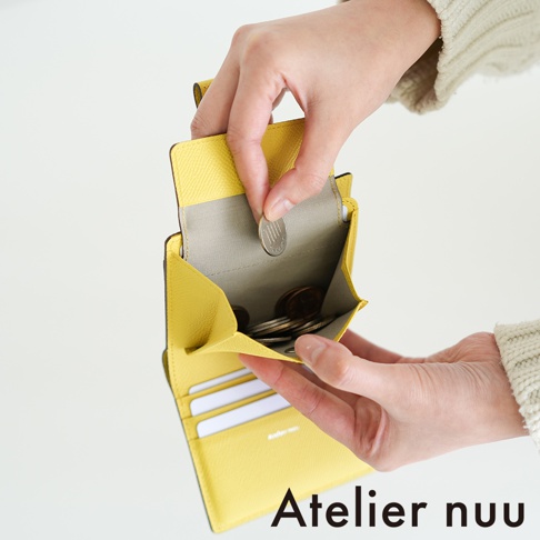 Atelier nuu 品牌字樣旁，一隻手正將日圓硬幣放入黃色皮革短夾的零錢袋中。