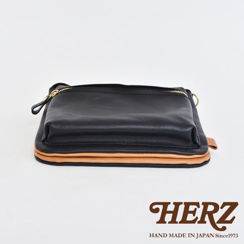 黑色皮革翻轉雙色直式斜背包，搭配裸色皮革層疊設計，金色拉鍊和金屬環細節。