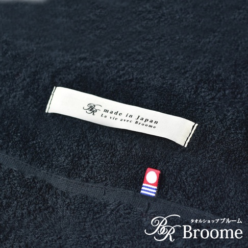 深藍色毛巾被，材質為柔軟的毛圈織物，表面可見「made in Japan」標籤及紅色、藍色條紋裝飾的小標誌。