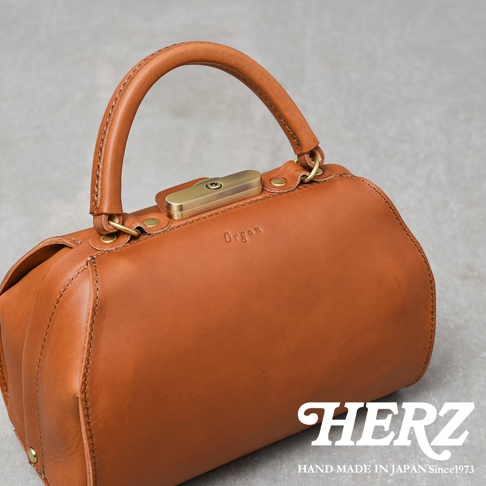 咖啡色皮革手提包，帶有金色金屬鎖扣和提把，包身壓印「Organ」字樣，風格簡約大方。