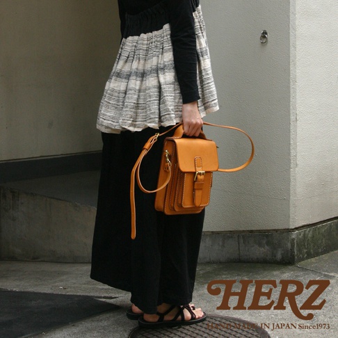 一位女士手提或側背一個由棕色皮革製成、帶有金屬扣的職人手作小方包。