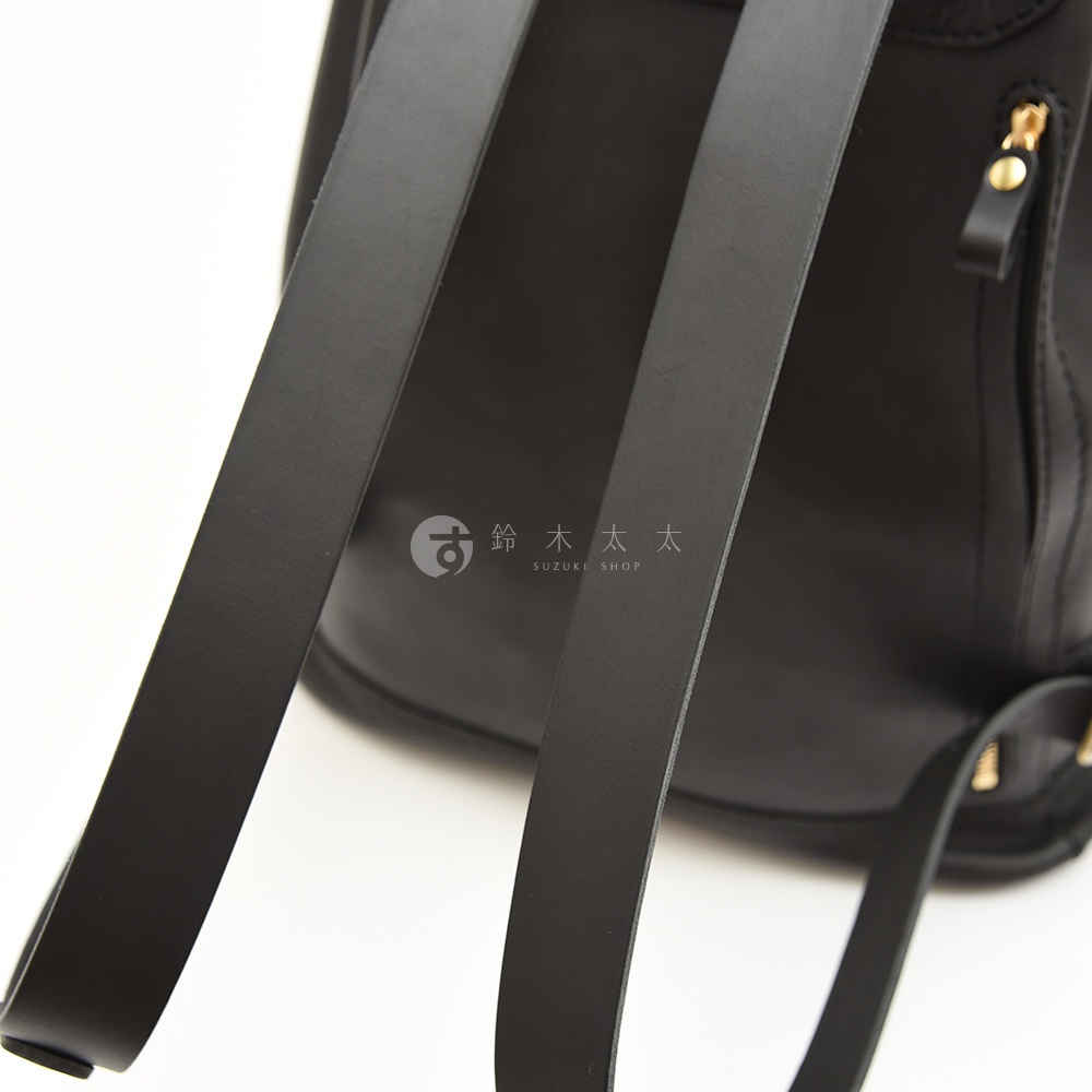 黑色皮革單扣束口後背包，有兩條寬版皮革背帶，背包側面有金色拉鍊和皮質拉頭。