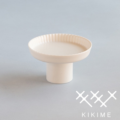 米白色陶瓷高腳平盤，盤緣有放射狀紋理，盤底為圓柱狀立體結構，設計簡約，適合盛裝點心或裝飾。