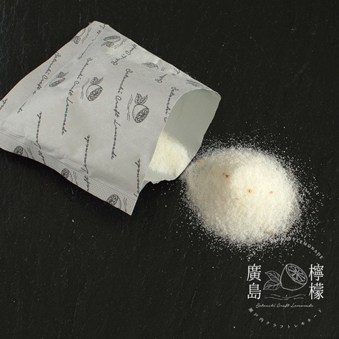 包裝精美的廣島檸檬粉末從印有檸檬圖案的小紙袋中傾倒而出，細緻的白色粉末堆疊在深色石板表面，右下角印有檸檬圖示與廣島檸檬字樣，整體呈現簡約質感的商品展示風格。