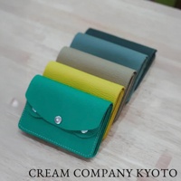 一排五個顏色鮮豔的皮革隨身零錢包，包括綠松石色、亮黃色、卡其色、藍綠色和深綠色，皆有銀色按扣。