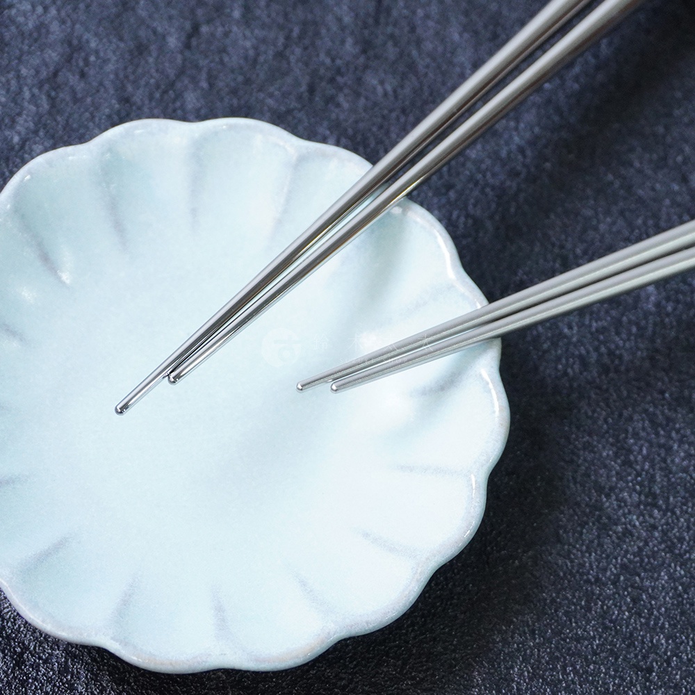 一組燕三條不鏽鋼筷子，共兩雙，筷子為銀色，材質為不鏽鋼，筷身光滑，末端為圓形。筷子擺放在一個淺藍色的扇形盤子上。