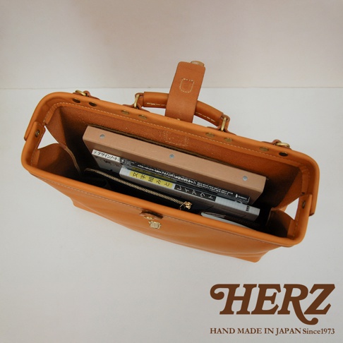 焦糖色皮革軟式杜勒斯包，內部裝有書籍和筆記本，包款開口處有金屬鎖扣和提把，整體呈現簡約復古風格。