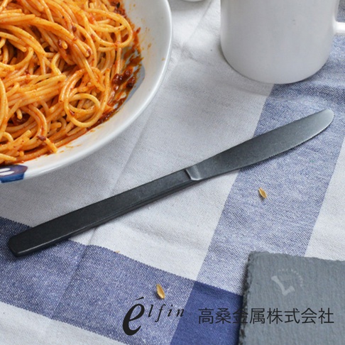 日製熔岩黑石餐刀，黑色金屬材質，餐刀呈水平放置，刀刃部分有細微鋸齒，刀柄為光滑平面設計。