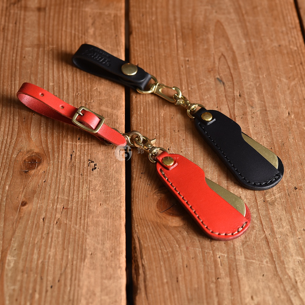 一紅一黑兩款職人手作皮革隨身金屬鞋拔，皆配有黃銅掛扣和金屬鞋拔，質感溫潤。