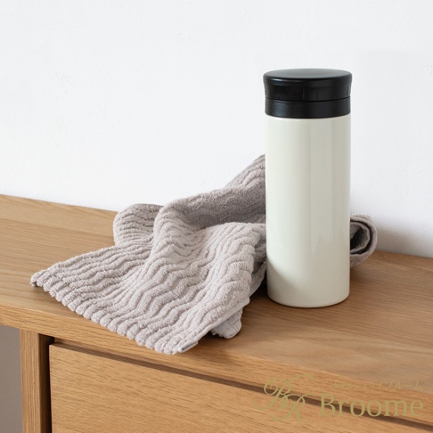Broome 品牌下的 ASH 今治柔韻波紋甘撚細毛巾，以淡奶油色保溫瓶和灰色毛巾擺放在木質桌面。