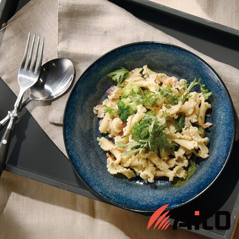 藍色漸層的義大利麵盤盛著色彩豐富的義大利麵，盤旁擺放著銀色的叉子和湯匙，整體呈現北歐自然風格。