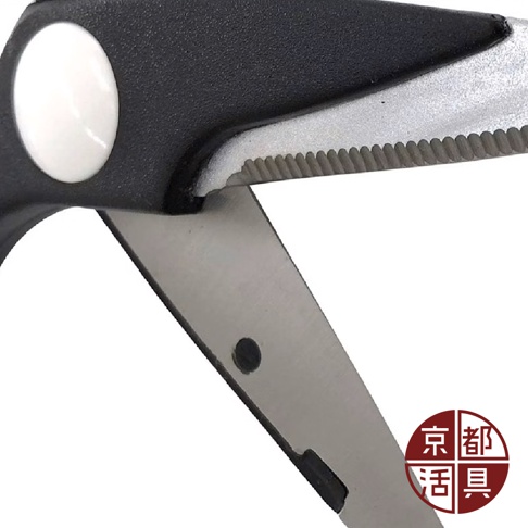 特寫展示不鏽鋼萬用料理剪刀的黑色握柄和部分刀刃，握柄上有一個圓形白色按鈕，刀刃邊緣有鋸齒狀設計，材質為不鏽鋼，部分刀面有反光。