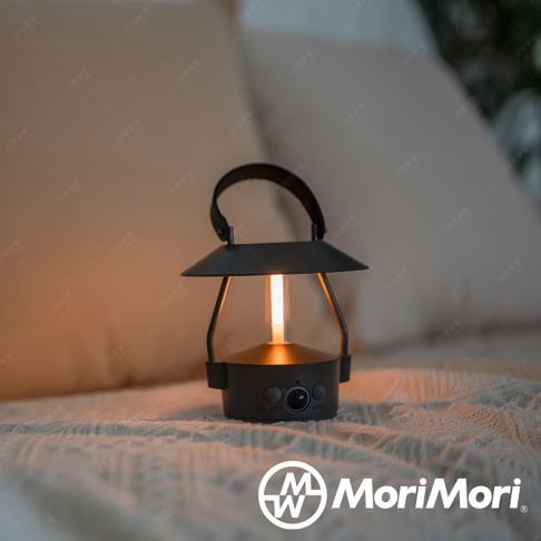 黑色MINIMO智慧感應LED燈，造型如復古提燈，頂部有提把，燈體下方有ON-OFF和AUTO按鈕，整體呈現溫暖燈光，放置於米白色織品上。