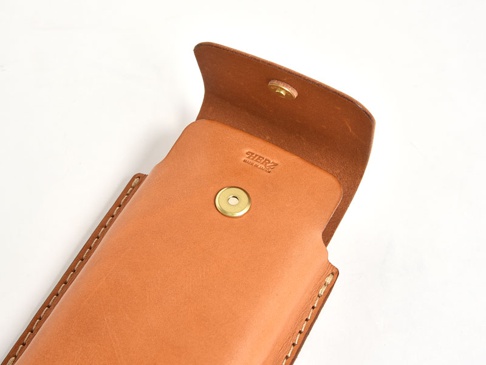 淺棕色皮革製成的手機收納包，開放式設計，可見品牌標誌「HERZ」及「MADE IN JAPAN」，配有金色按鈕。
