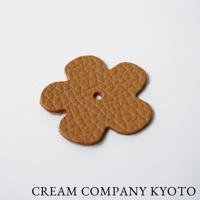 淺棕色皮革製成的五瓣花形吊飾，表面有菱格紋壓紋，中央有一小圓孔。