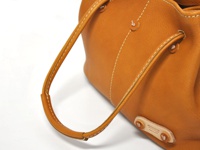 焦糖色皮革托特包，附有可調式提把，採用白色縫線裝飾，底部有品牌標誌。