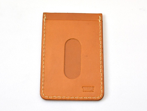 一個直式淺棕色皮革票券收納夾，正面有一個橢圓形透明視窗，縫線清晰，右下角壓印有「HERZ MADE IN JAPAN」字樣。