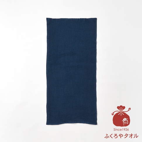 深藍色格子紋理的浴巾，角落有紅色袋狀圖案標誌，標誌下方有Since1926字樣及日文ふくろやタオル。