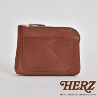 一個棕褐色的職人手作皮革小物收納包，正面有一個方形的貼袋，袋上有品牌壓印。包包上方有金屬拉鍊，皮革邊緣有縫線，整體呈現簡約風格。