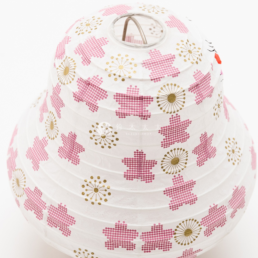 白色紙質達摩不倒翁提燈，表面印有粉色星形圖案與金色放射狀小花圖案，提燈頂部有金屬提環，側邊可見達摩的臉部特徵。