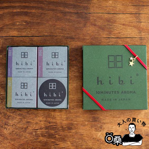 左邊為四小盒灰色包裝的香氛火柴，分別印有「002 Lavender」、「000 Yuzu」、「007 Citrus」和「000 Yuzu」字樣。右邊為一盒綠色包裝的香氛火柴禮盒，以紅色緞帶繫住，並綴有金色星星吊飾，禮盒上印有「hibi 10MINUTES AROMA MADE IN JAPAN」字樣。