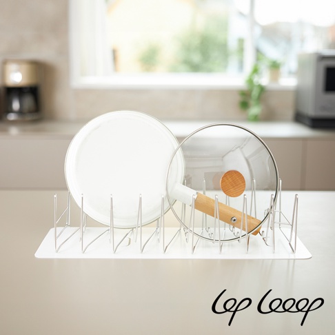 銀色不鏽鋼線條構成的伸縮式瀝水架，架上擺放一個白色圓盤和一個玻璃鍋蓋，鍋蓋帶有木質手柄。瀝水架下方為白色防水墊。