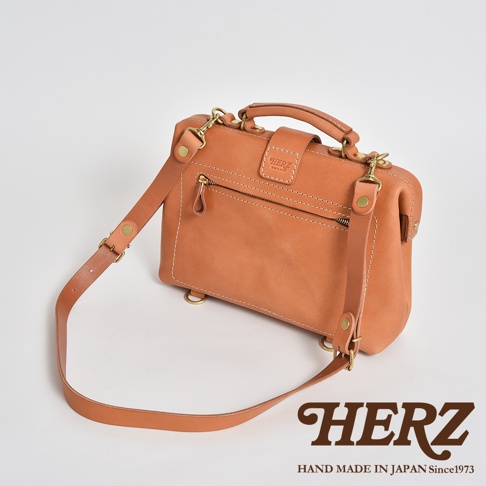 一個棕褐色軟皮迷你杜勒斯包，配有頂部提把、可拆卸肩帶、拉鍊口袋和金色五金件。