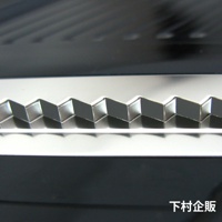 銀色金屬材質的四合一刨絲器，展示其鋸齒狀的刀刃特寫，刀刃呈 Zig-zag 形狀，表面光滑反光，呈現出精緻的工藝細節。