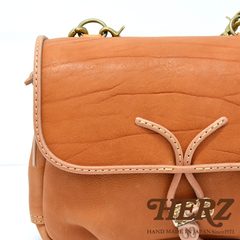 職人手作皮革鹿角扣繩郵差包，採用天然皮革材質，呈現溫潤的棕褐色，包身帶有自然的皮革紋路，並有皮革繩和金屬扣環裝飾，風格復古。