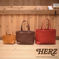 三款皮革托特包，由左至右分別為淺棕色、深棕色及紅色，皆為簡約的四口袋設計，材質光滑，配有同色系提把，整體呈現質感。