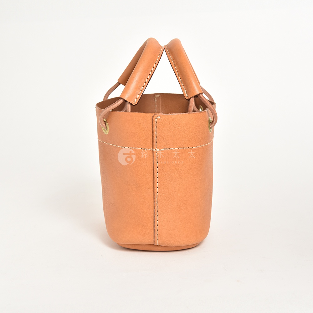 淺棕色皮革製成的職人手作提把午餐袋，圓筒形設計，大開口，車縫線明顯，附有金屬孔眼與束繩。