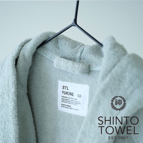 淺藍色 YUKINE 有機棉蓬厚浴袍，掛於黑色衣架上，衣領處有白色標籤，標示「ORGANIC COTTON 100%」及「SHINTO TOWEL, MADE IN JAPAN」。