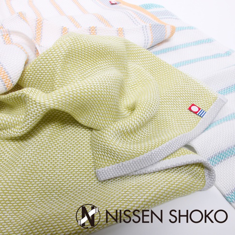 一條淺黃綠色今治純棉廚房擦拭巾，織有細緻紋理，邊緣有灰色滾邊。背景疊放著其他同系列擦拭巾，帶有橘色、藍色條紋。