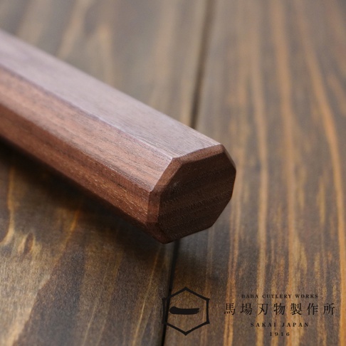 [景清] Chromax鋼三德刀的胡桃木刀柄，呈現溫潤的木紋與八角造型，置於深色木紋背景上。
