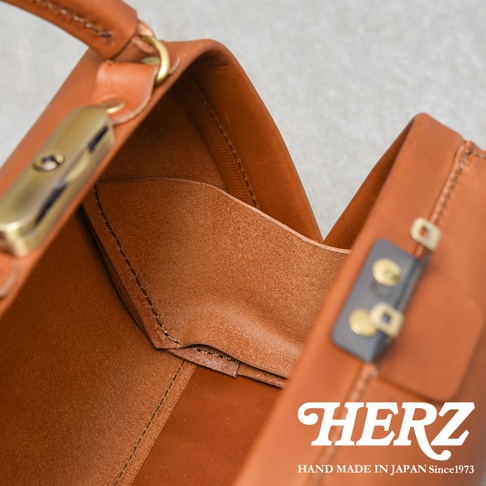 職人手作皮革Organ兩用口金手提包，展示包包內部結構，採用光滑的棕色皮革製作，配有金色金屬扣件和細緻縫線。