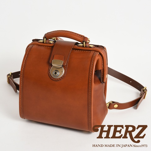 職人手作棕色皮革迷你後背醫生包，包身方正，頂部有提把，前方有金屬旋轉鎖扣，附有可調節皮革背帶。