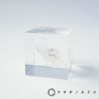 透明立方體壓克力中封存著一塊天然白水晶，水晶呈現半透明狀，內部帶有細微雜質與紋理，整體色調為白色與透明。