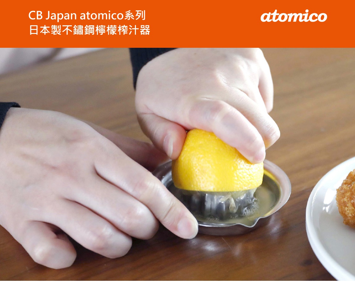 CB Japan atomico系列日本製不鏽鋼檸檬榨汁器，一隻手正將半顆檸檬壓在金屬榨汁器上，另一隻手輔助固定，榨出新鮮檸檬汁。