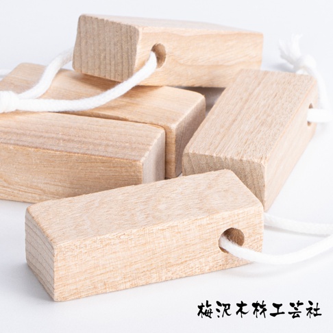 數塊天然淺棕色樟木條，每塊皆有穿孔，並穿有白色棉繩，部分木條堆疊，呈現自然紋理。