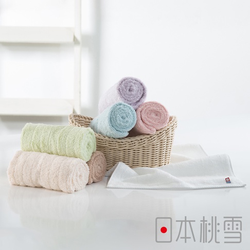 一籃五條捲起的今治超長棉毛巾，顏色包含淺紫、淺藍、粉紅。籃子旁另有三條捲起的毛巾，顏色為淺綠、淺粉紅和淺棕色。右側為一條展開的白色毛巾。