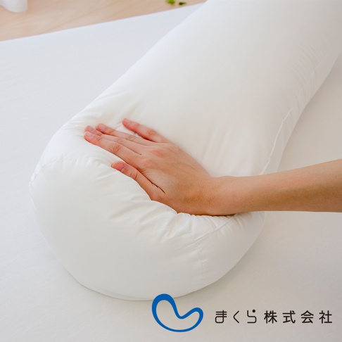 白色圓柱形夾腿枕，表面為光滑織物材質，枕套可拆卸。手部輕柔按壓枕頭，展現其柔軟度。