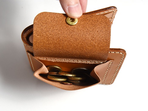職人手作的棕色皮革雙折短夾，外附有零錢袋，零錢袋內裝有幾枚硬幣。皮革表面紋理清晰，縫線整齊。