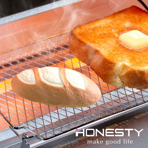 烤箱架上放置著一個小型法式長棍麵包，麵包呈淺棕色，表面有三道白色壓痕。一旁是一片烤得金黃的吐司，上面融化著一塊奶油。烤箱內的加熱管發出橘紅色光芒，並有細微的蒸氣。