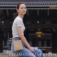 一位女性斜挎著一個淺褐色皮革材質的隨身手機包，包包設計簡約，正面有一個銀色圓形按扣。