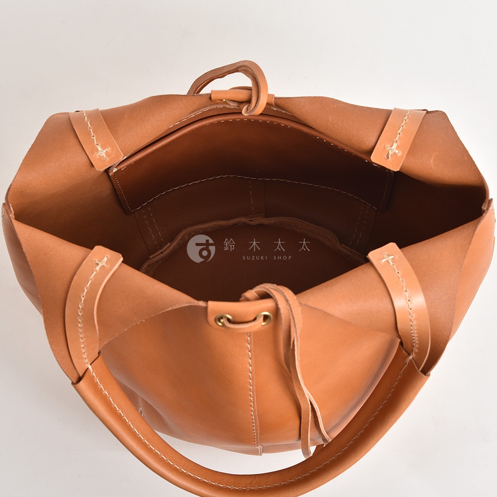 一個棕褐色皮革製成的球形托特包，頂部開口，內有隔層，配有圓形提把和可調節肩帶，邊緣有縫線裝飾。