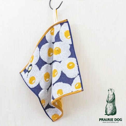 一塊印有煎蛋圖案的藍色毛巾，四周鑲有黃色滾邊，毛巾上掛著一個小鍋的圖案，右下角有一個站立的土撥鼠插畫。