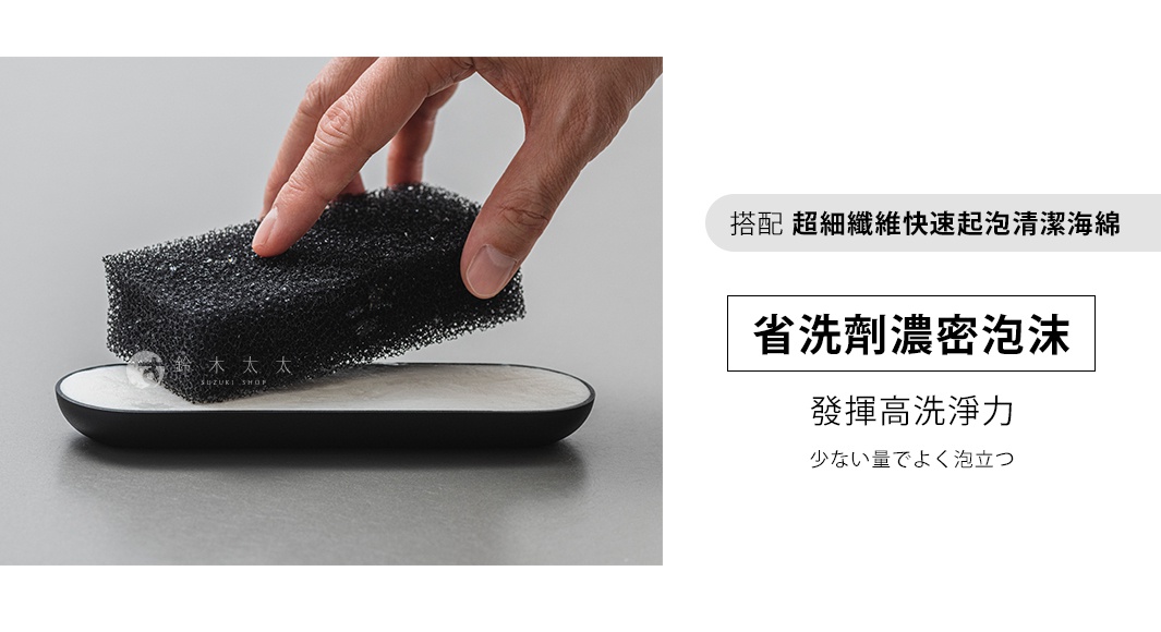 一隻手拿著黑色海綿，置於一個白色有淺灰色紋理的橢圓形皂盤上，皂盤邊緣為黑色。