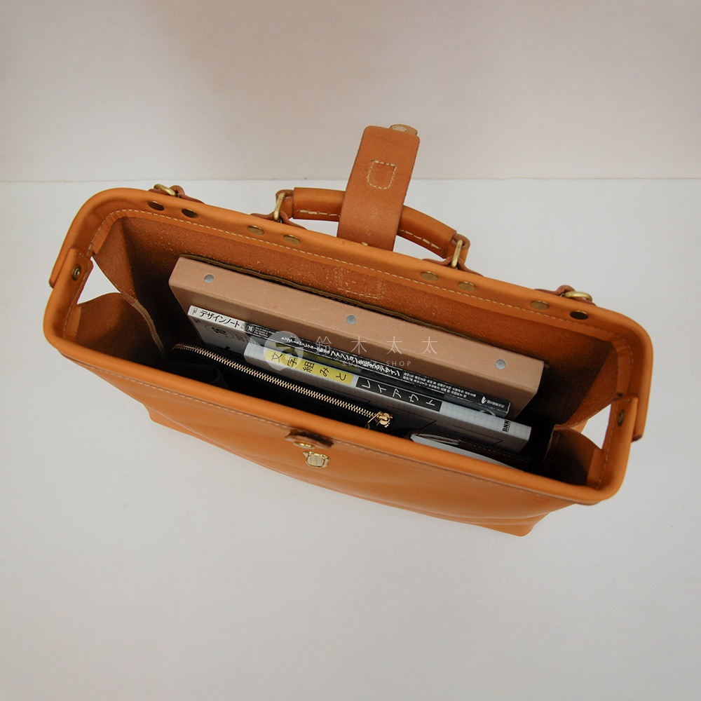 職人手作皮革軟式杜勒斯包，呈現溫潤的焦糖色調，包身結構紮實，內部裝有書籍和筆記本，展現其收納功能。